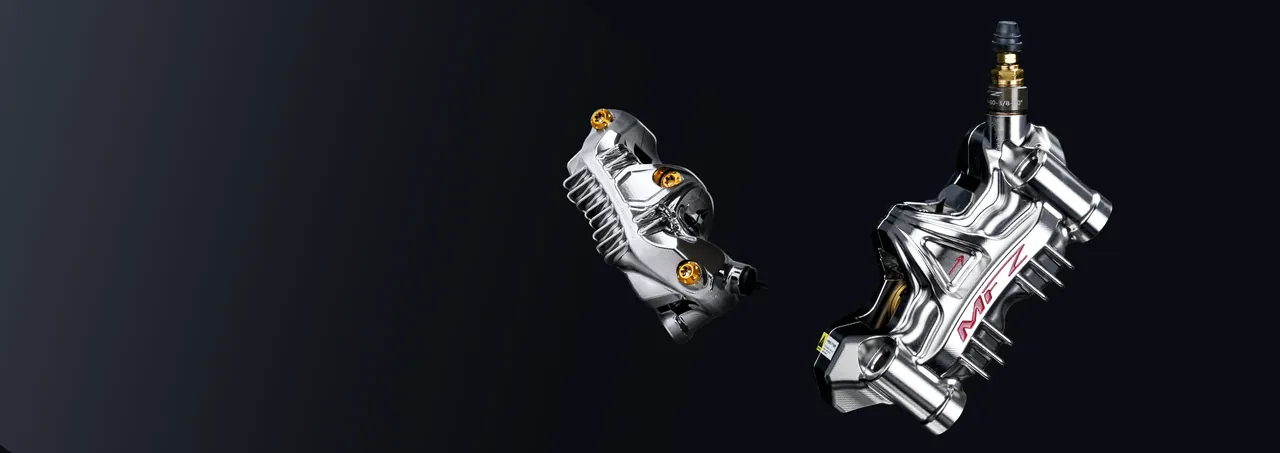 Two polished radial brake calipers photographed on a dark gray background