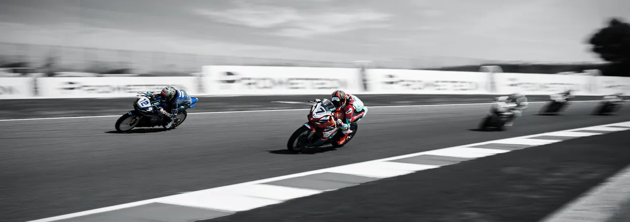 Riders leaned over on a racetrack in black and white